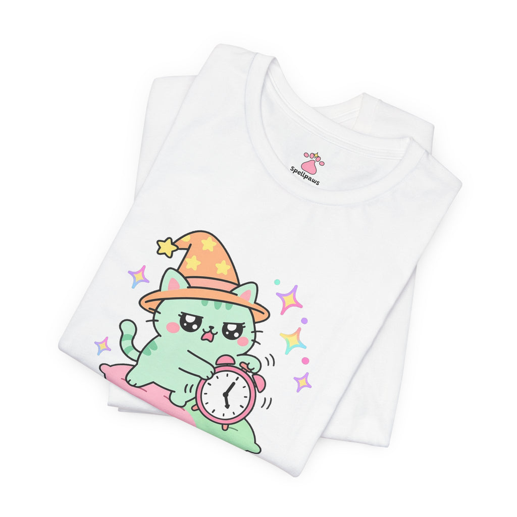 Folded white Alarmus Felinus T-shirt showing a close-up of the mint-green wizard cat in an orange hat on a pink pillow, pawing a ringing alarm clock