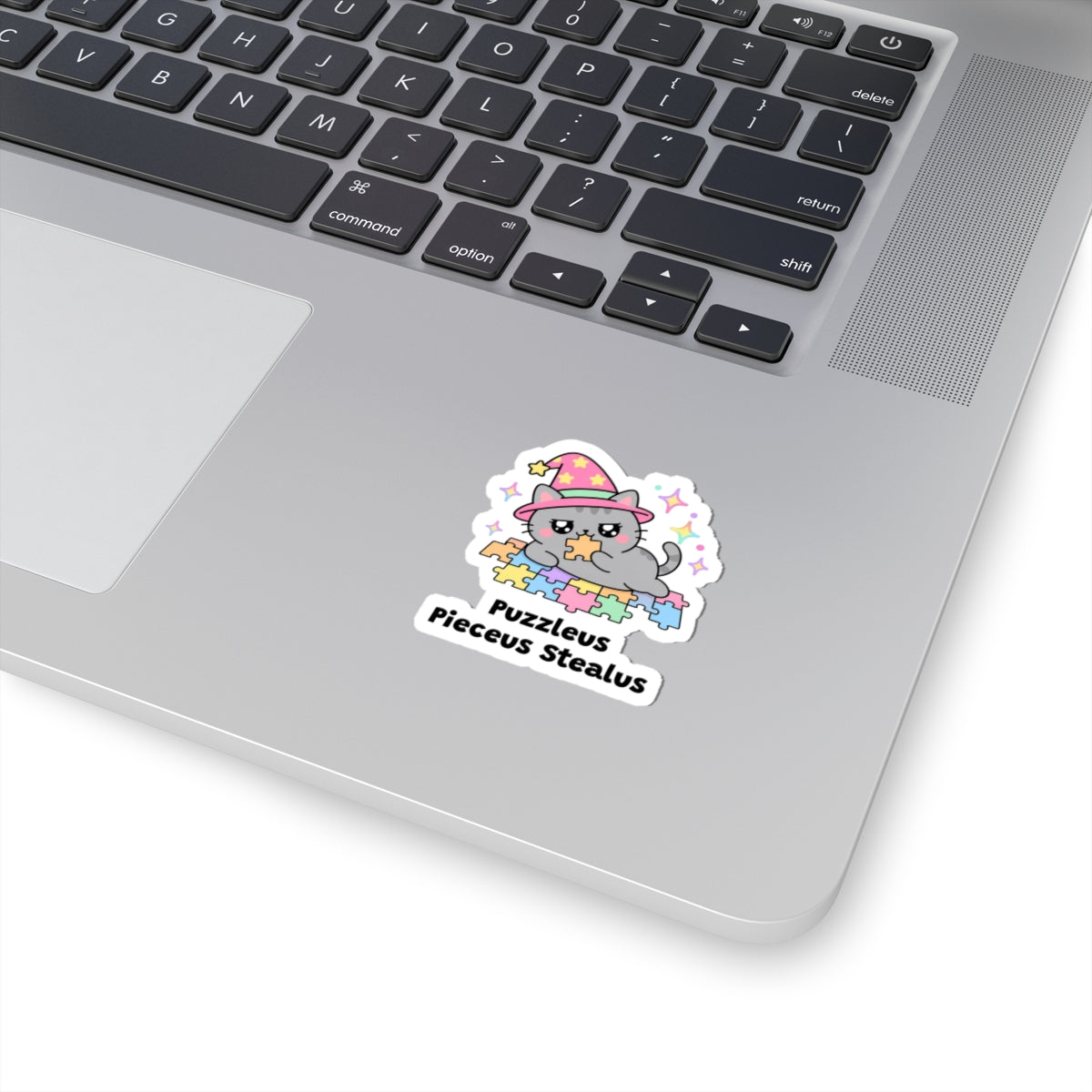 Puzzleus Pieceus Stealus wizard cat sticker stuck on a silver laptop next to the keyboard