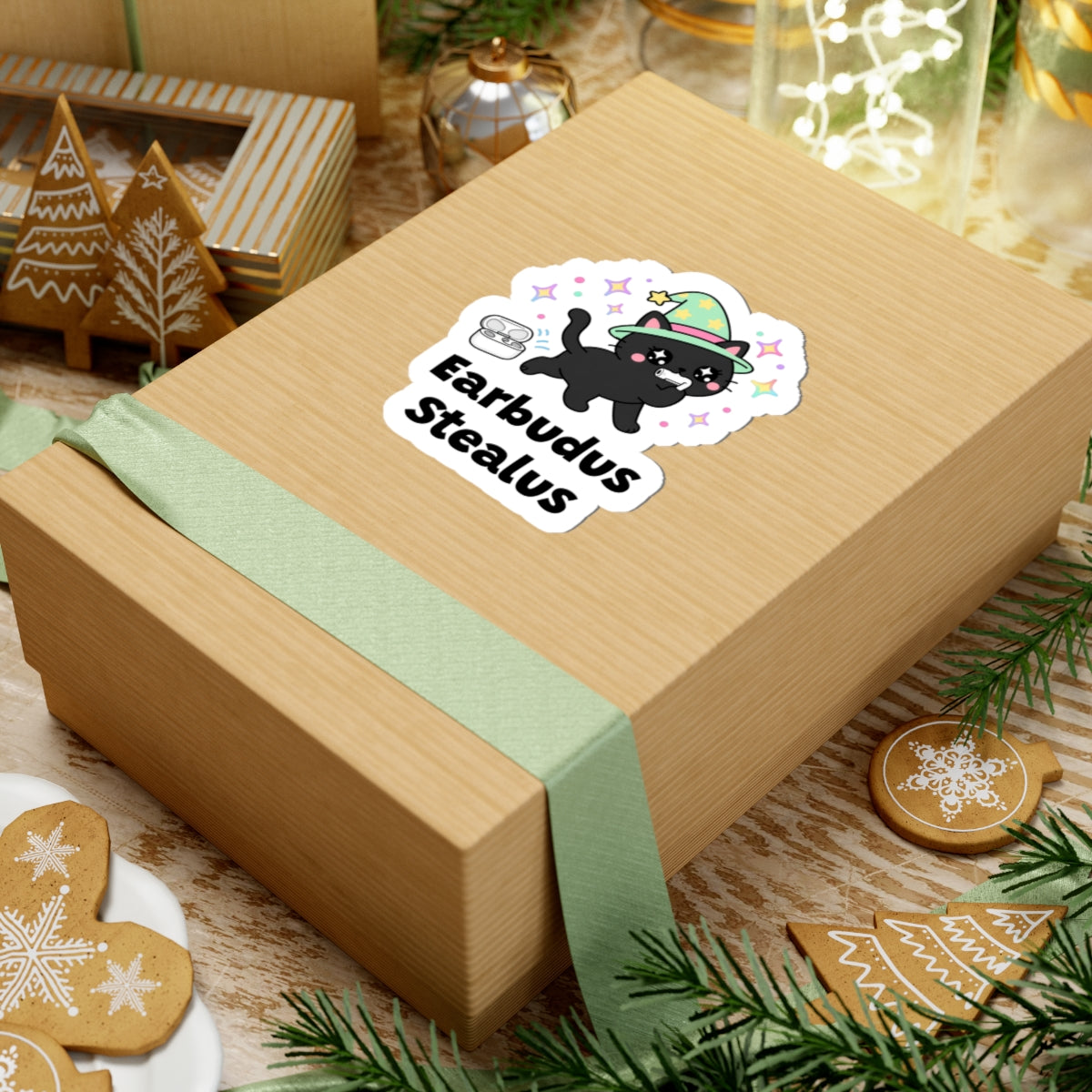 Earbudus Stealus wizard cat sticker on a kraft gift box with a green ribbon and holiday cookies
