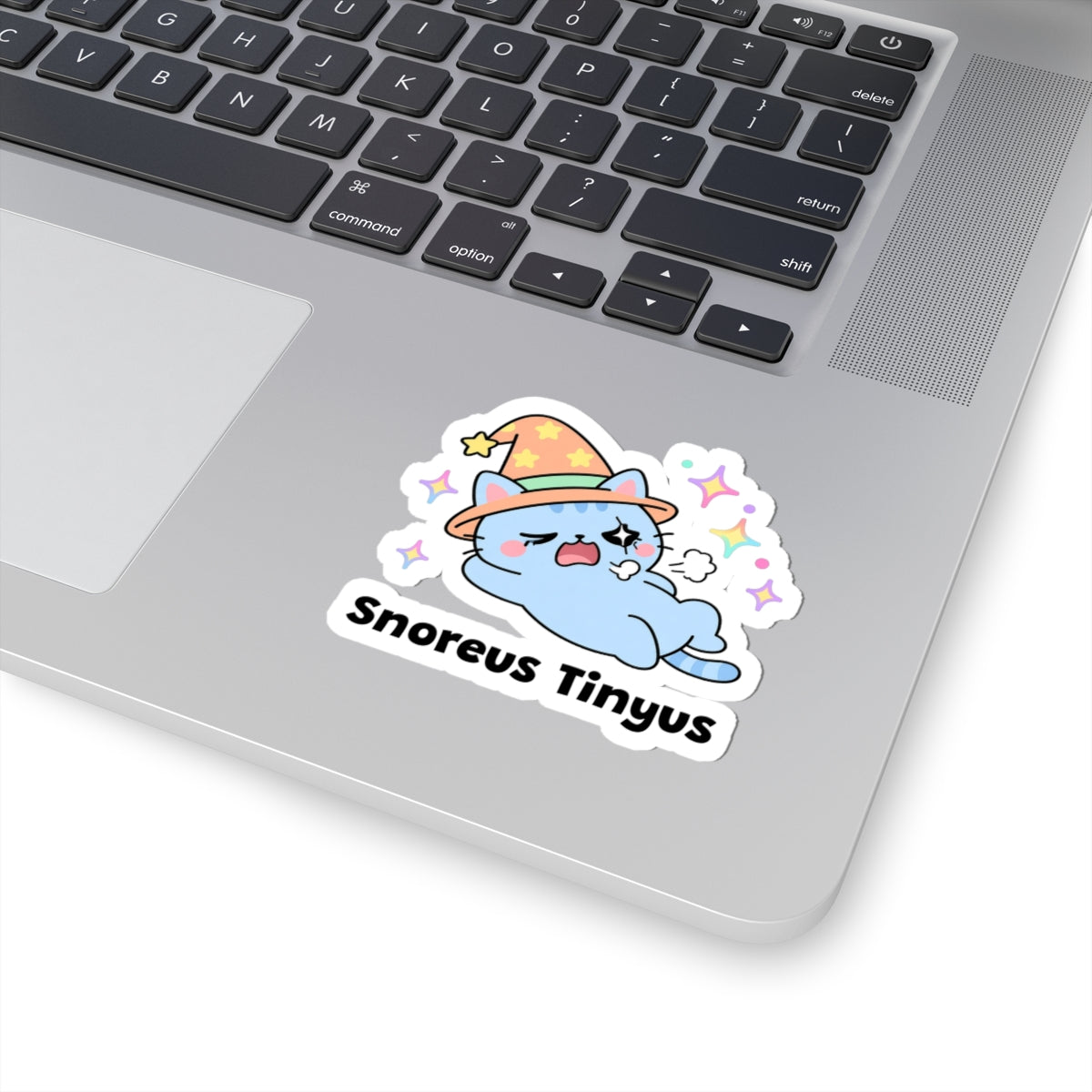 Snoreus Tinyus wizard cat sticker stuck on a silver laptop next to the keyboard