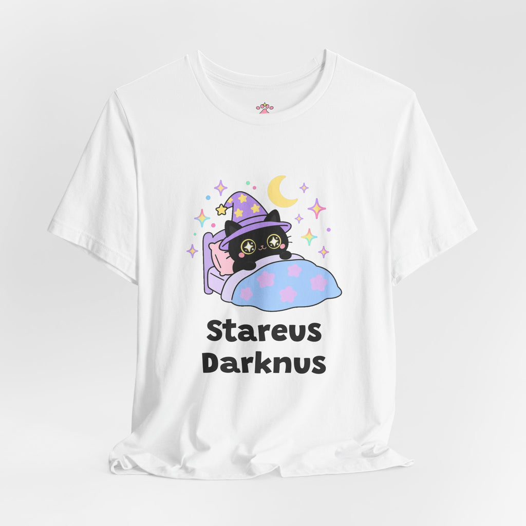 White Stareus Darknus wizard cat T-shirt shown in a soft studio setting: black wizard cat in a purple hat with glowing star eyes peeking over a blue blanket under a crescent moon