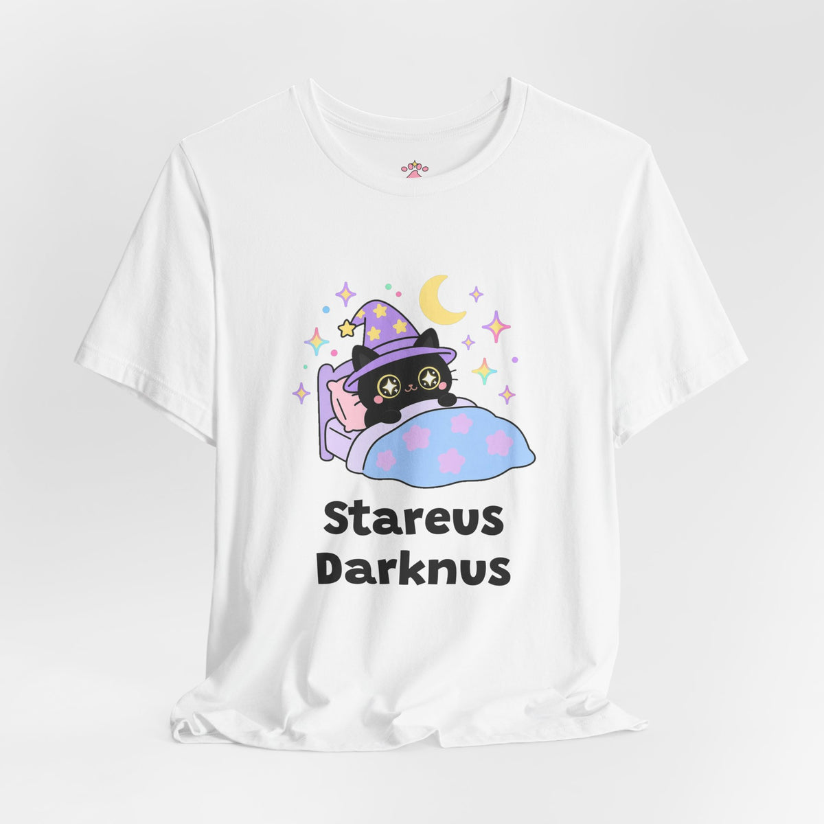 White Stareus Darknus wizard cat T-shirt shown in a soft studio setting: black wizard cat in a purple hat with glowing star eyes peeking over a blue blanket under a crescent moon