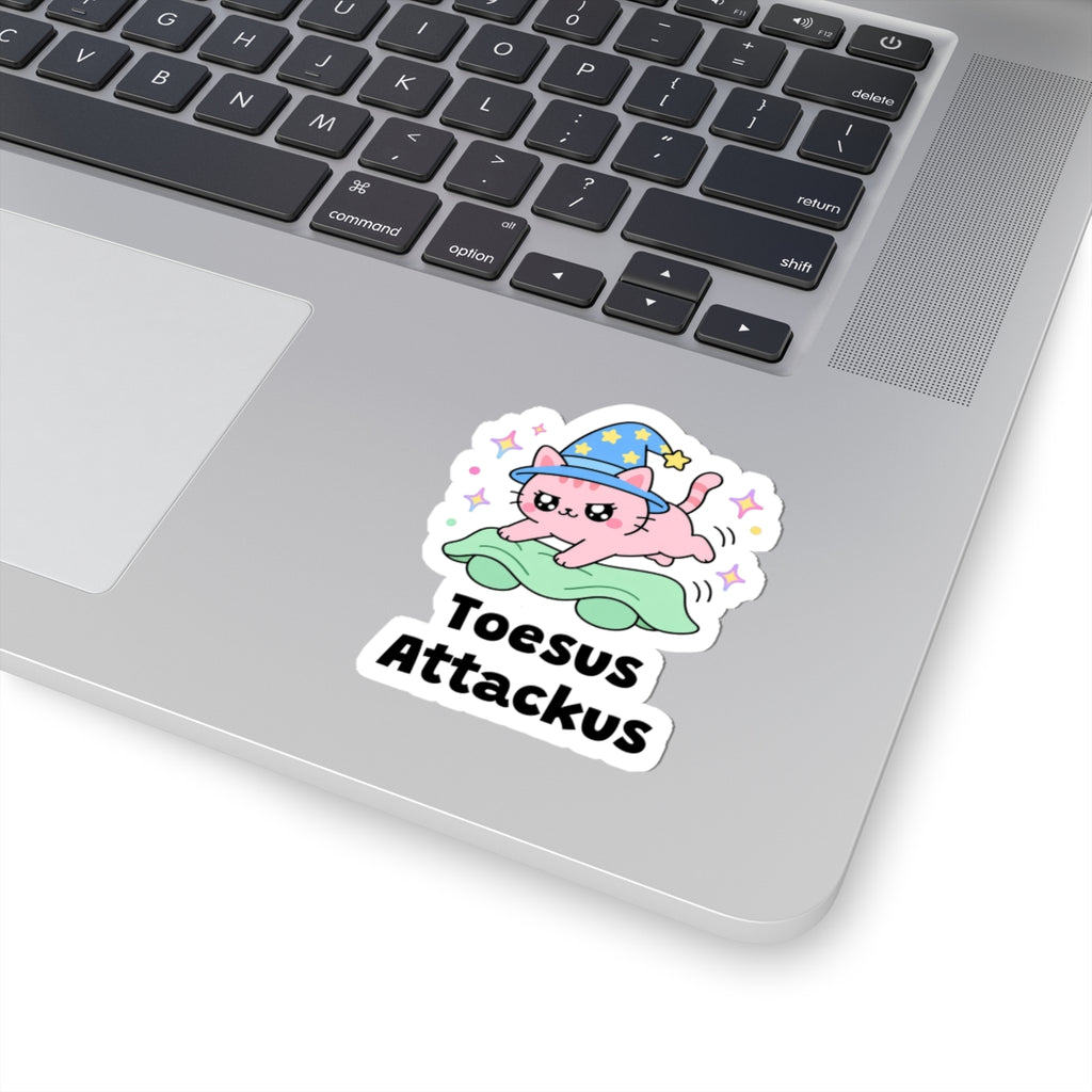 Toesus Attackus wizard cat sticker stuck on a silver laptop next to the keyboard