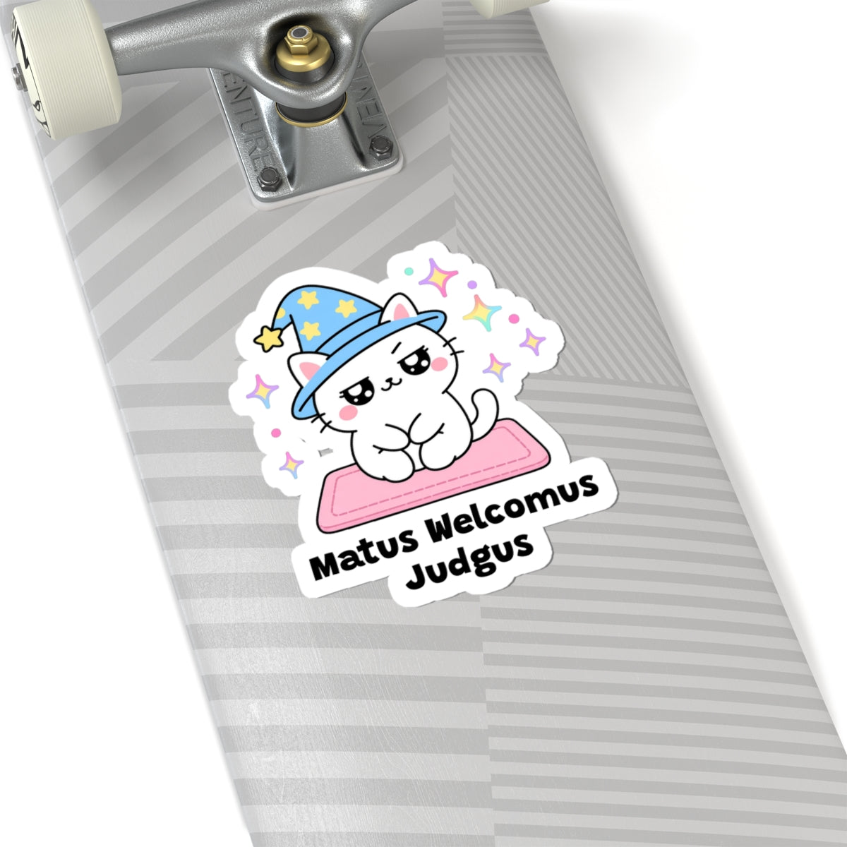 Matus Welcomus Judgus wizard cat sticker on a grey skateboard deck near the truck
