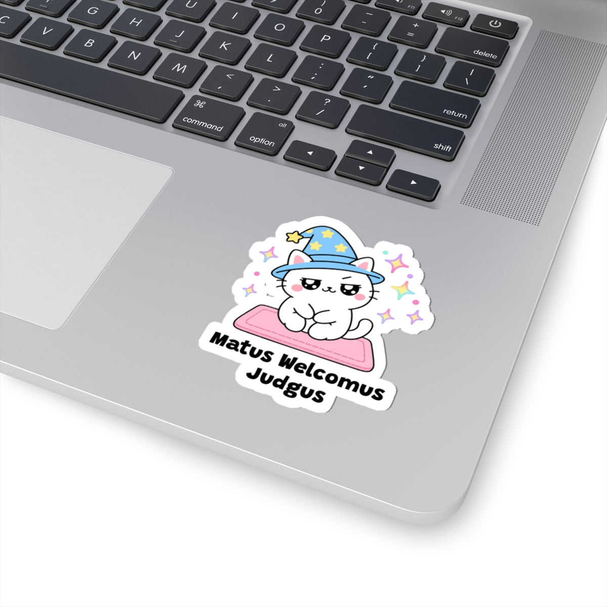 Matus Welcomus Judgus wizard cat sticker stuck on a silver laptop next to the keyboard