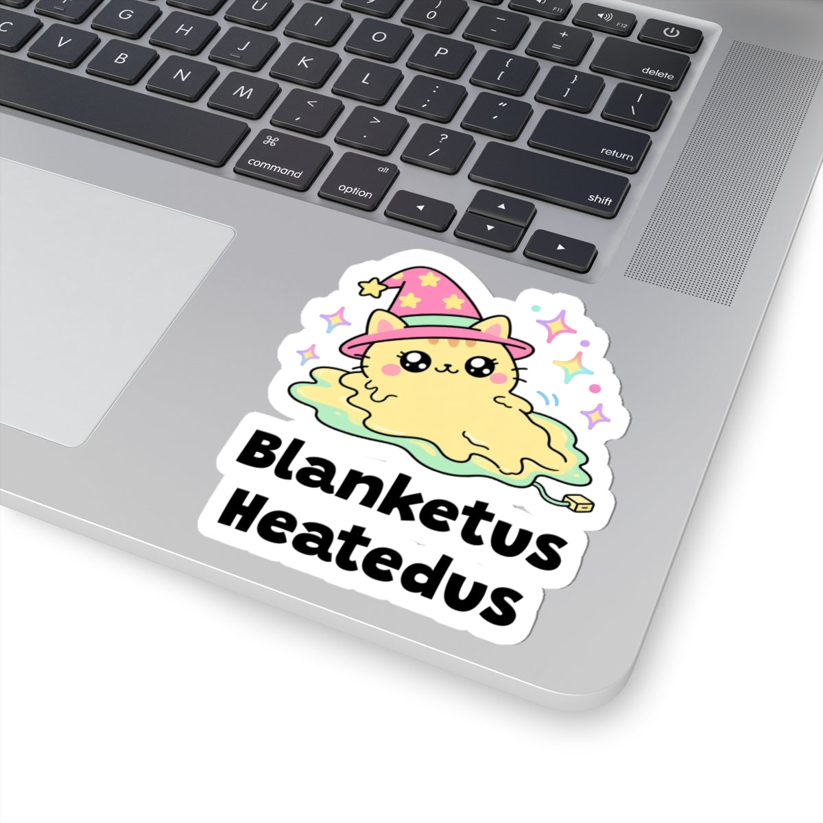 Blanketus Heatedus wizard cat sticker stuck on a silver laptop next to the keyboard