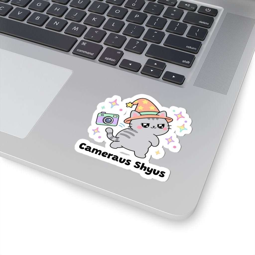 Cameraus Shyus wizard cat sticker stuck on a silver laptop next to the keyboard