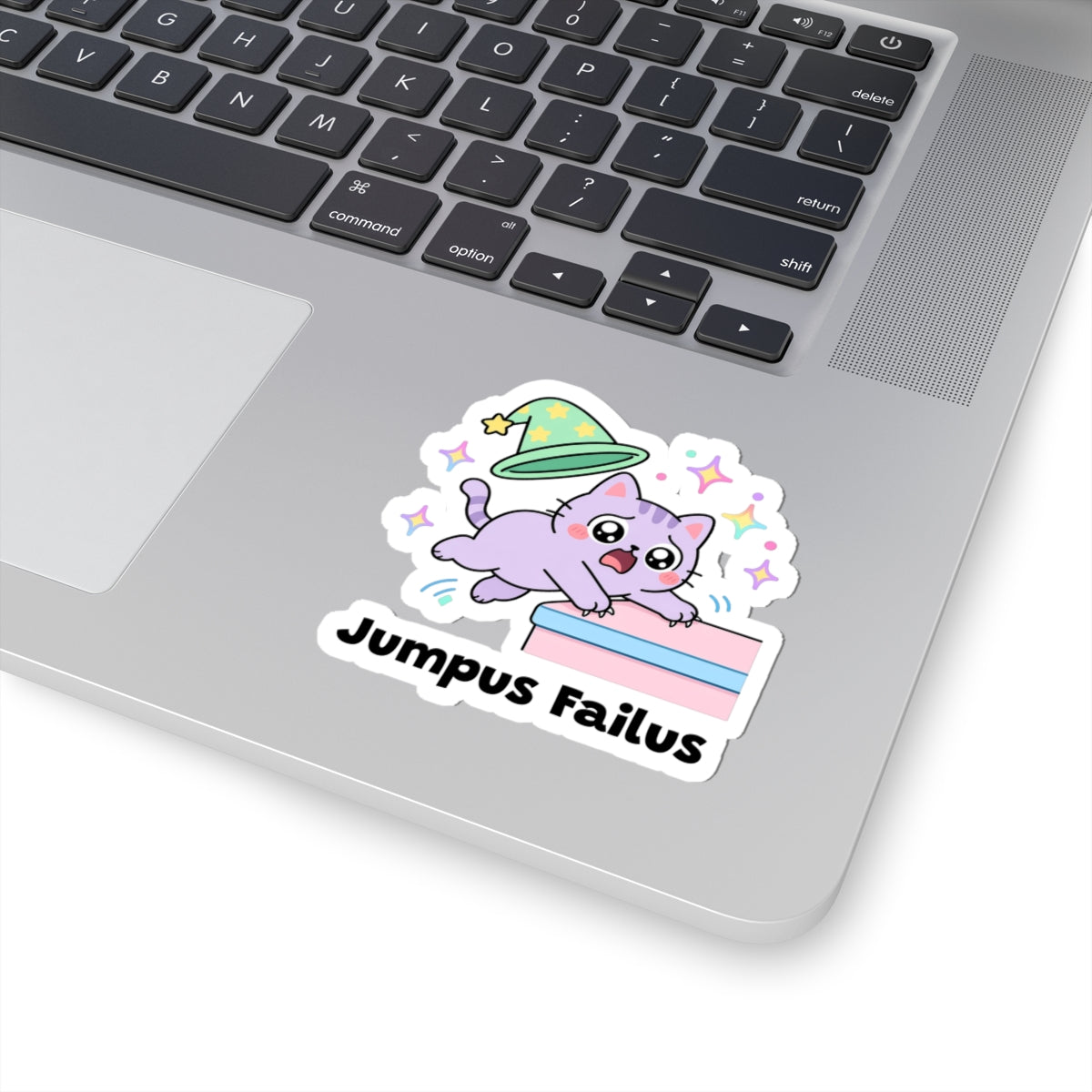 Jumpus Failus wizard cat sticker stuck on a silver laptop next to the keyboard