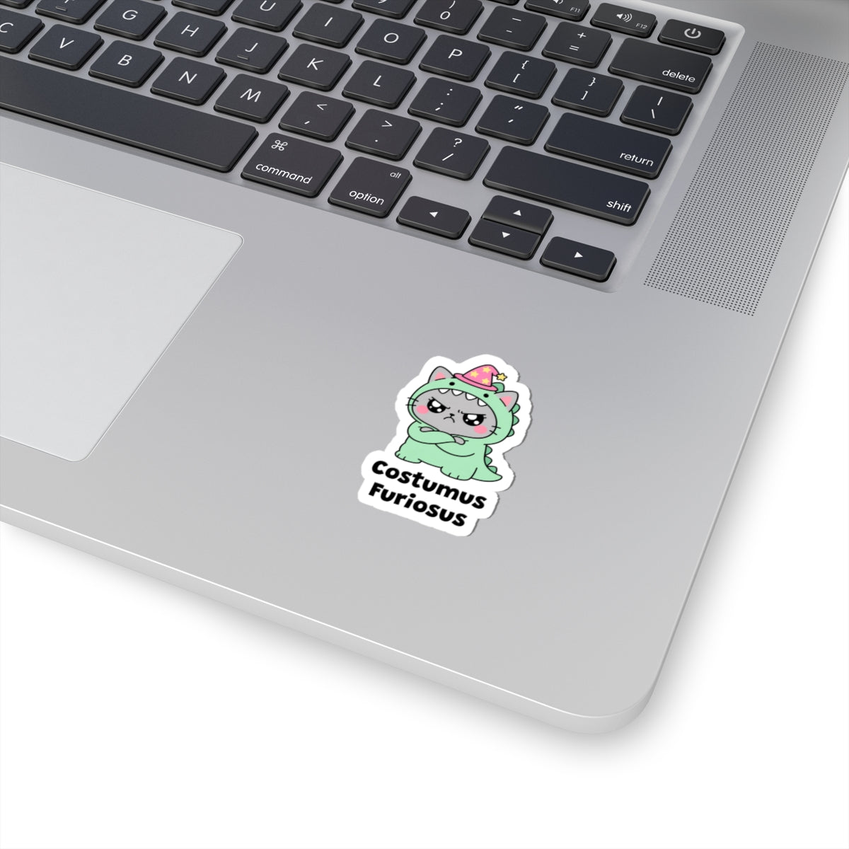 Costumus Furiosus wizard cat sticker stuck on a silver laptop next to the keyboard