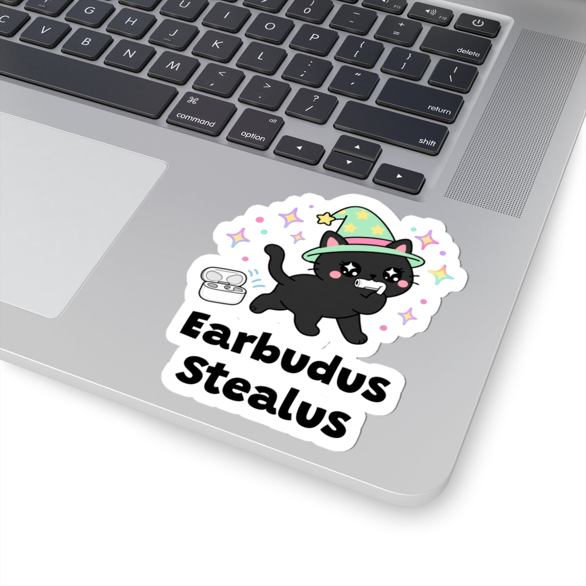 Earbudus Stealus wizard cat sticker stuck on a silver laptop next to the keyboard