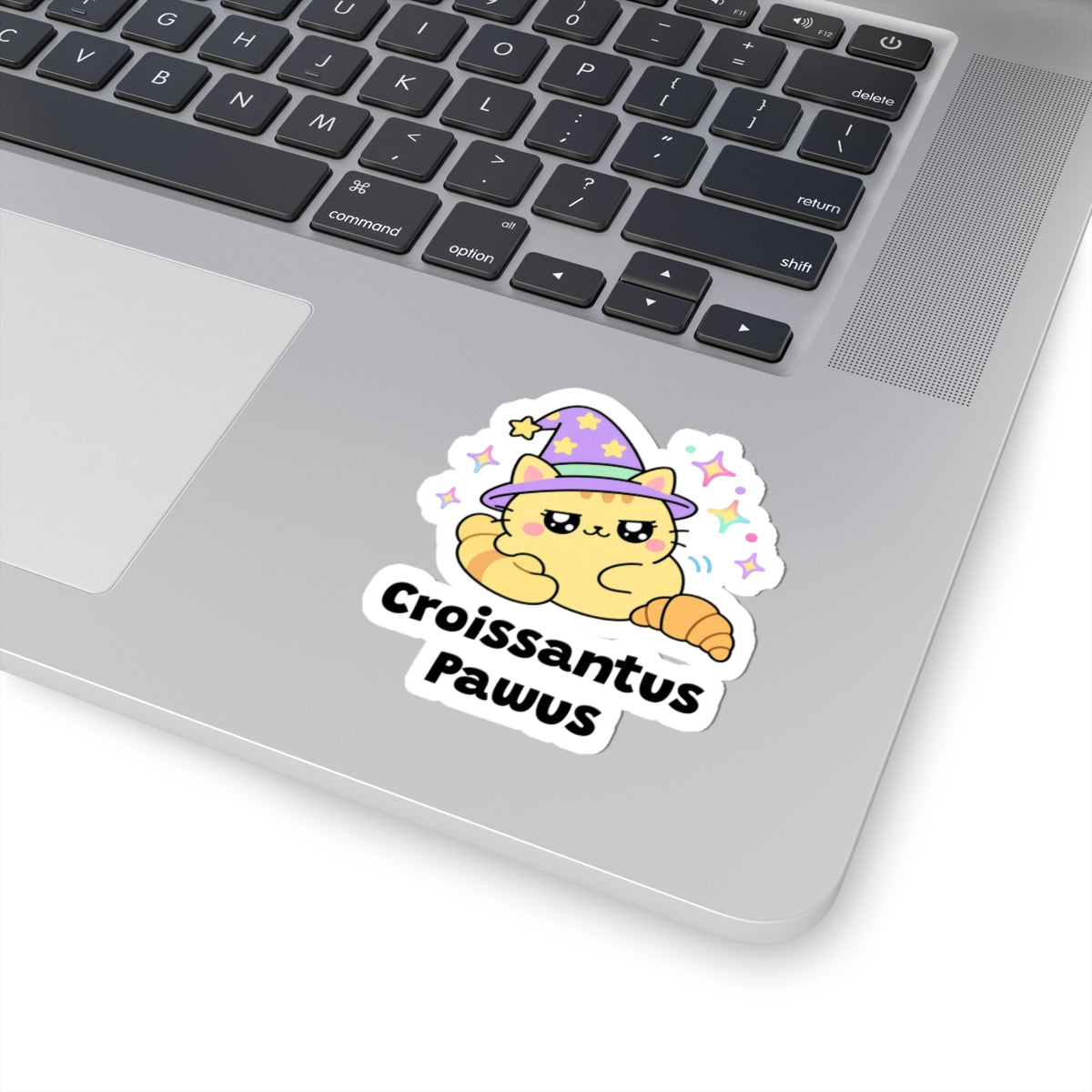 Croissantus Pawus wizard cat sticker stuck on a silver laptop next to the keyboard
