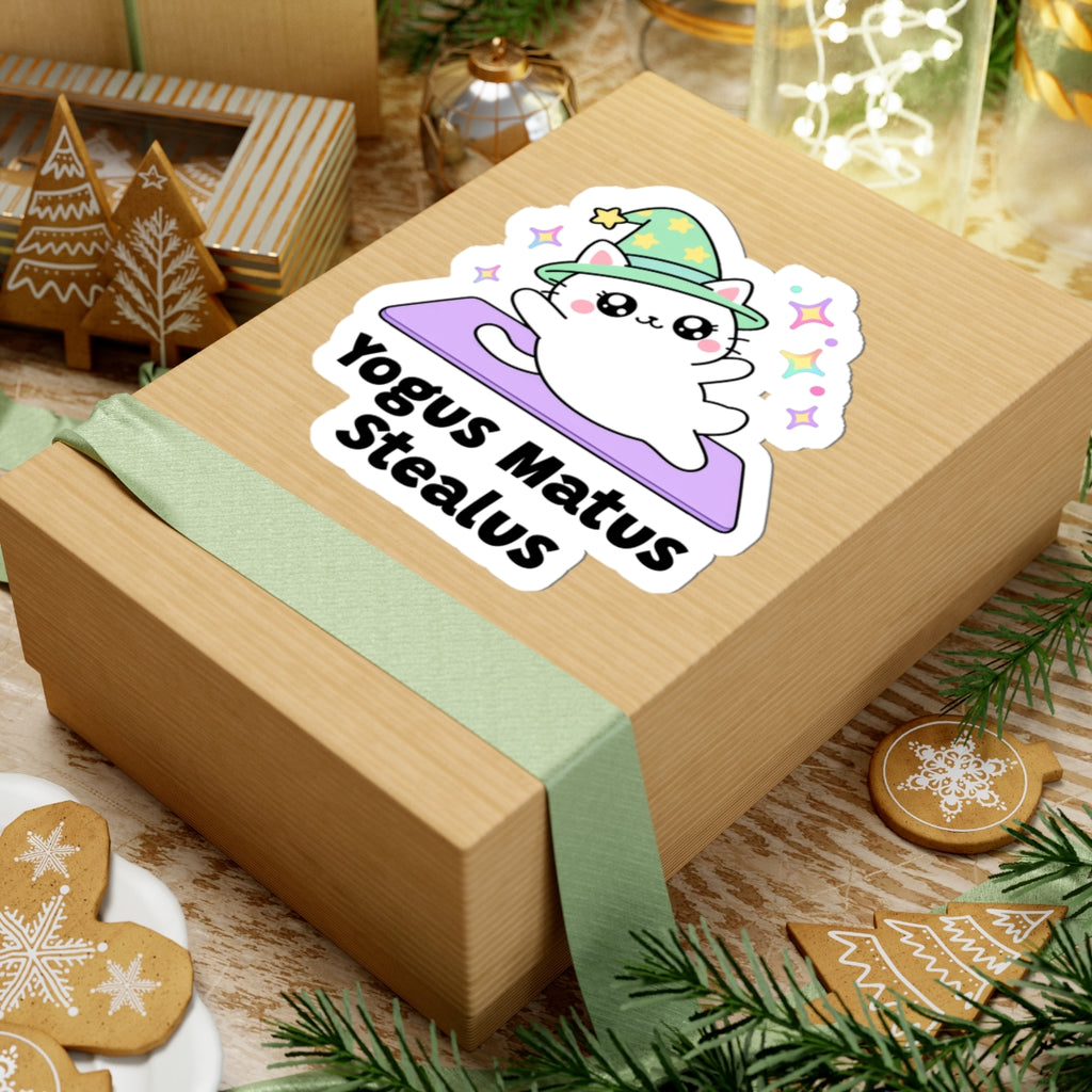 Yogus Matus Stealus wizard cat sticker on a kraft gift box with a green ribbon and holiday cookies