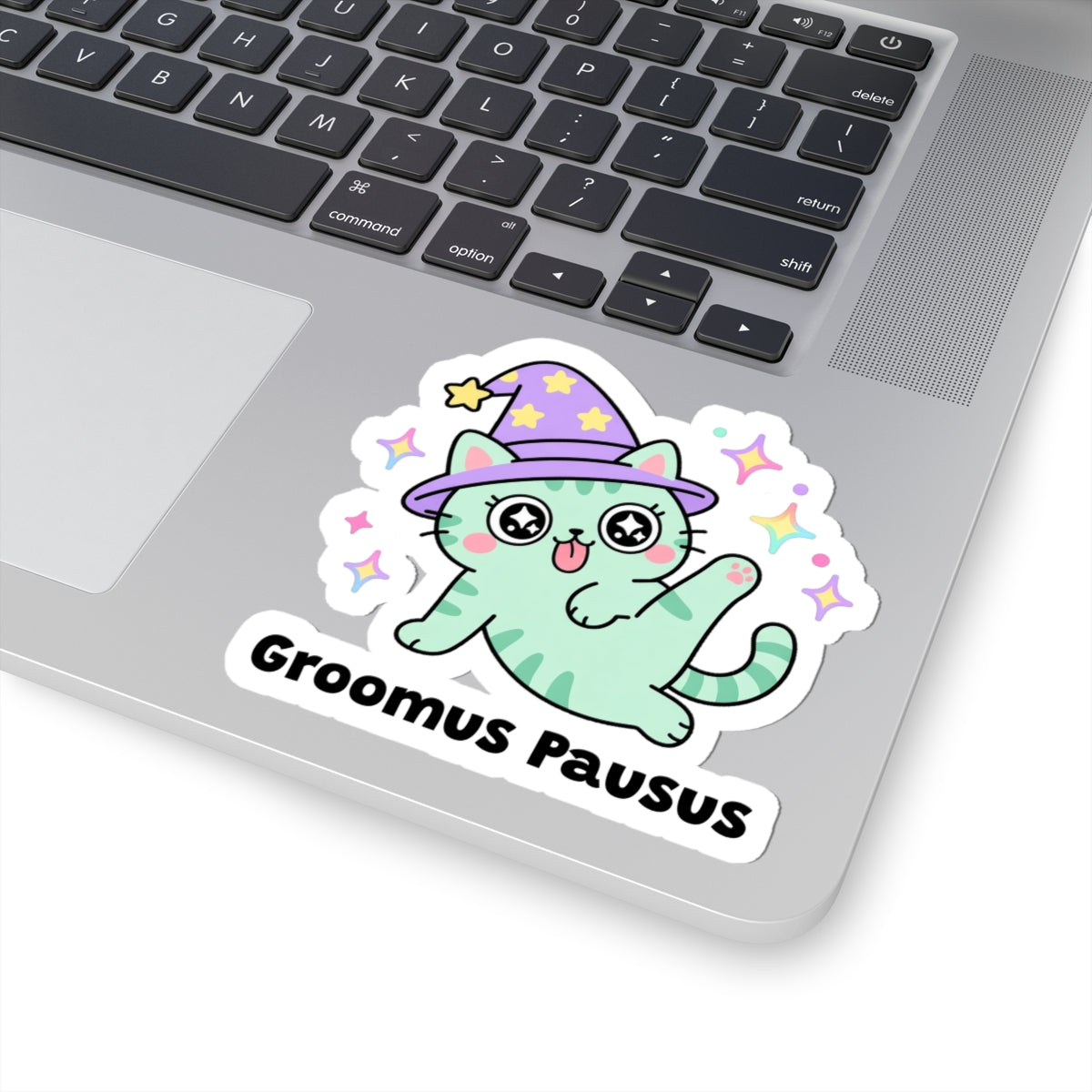 Groomus Pausus wizard cat sticker stuck on a silver laptop next to the keyboard