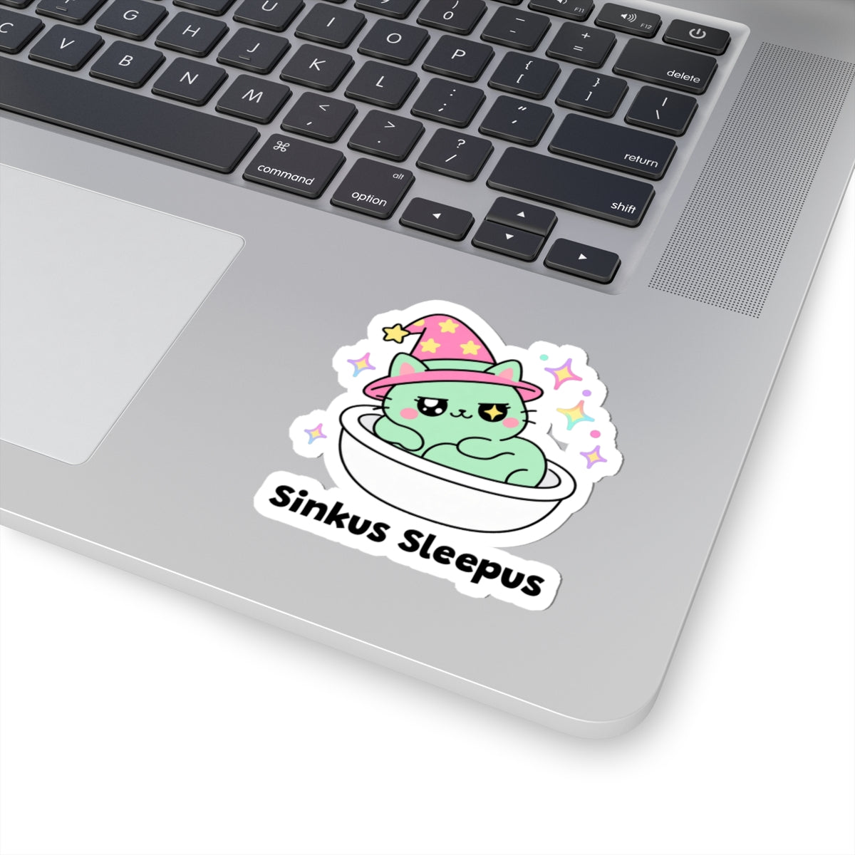 Sinkus Sleepus wizard cat sticker stuck on a silver laptop next to the keyboard