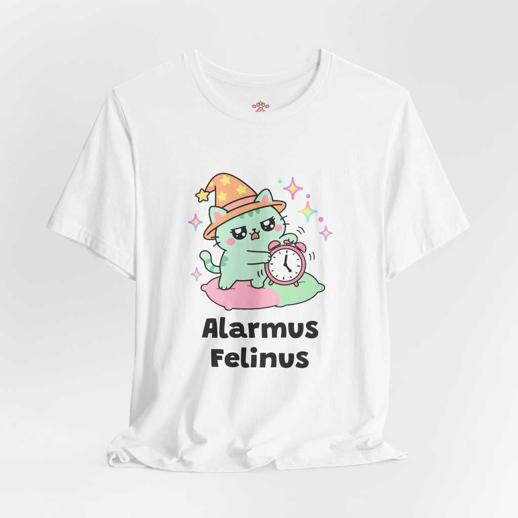 White Alarmus Felinus wizard cat T-shirt shown in a soft studio setting: mint-green wizard cat in an orange hat on a pink pillow, pawing a ringing alarm clock