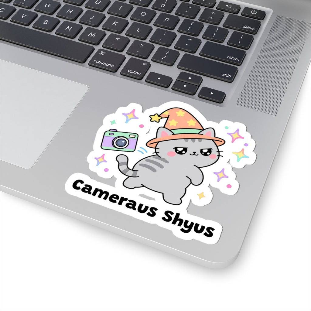 Cameraus Shyus wizard cat sticker stuck on a silver laptop next to the keyboard
