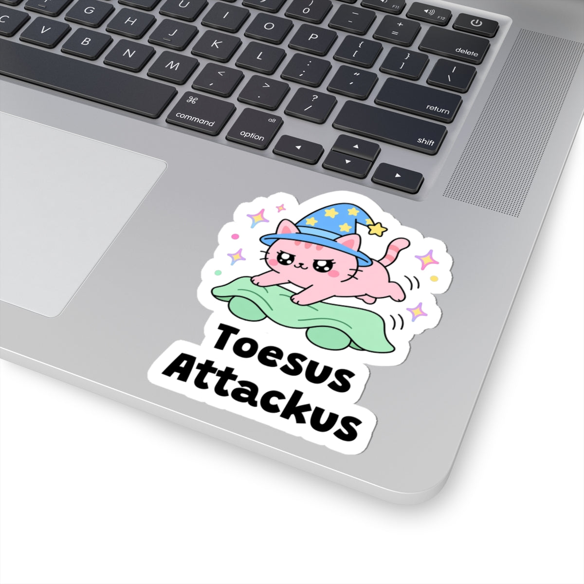 Toesus Attackus wizard cat sticker stuck on a silver laptop next to the keyboard