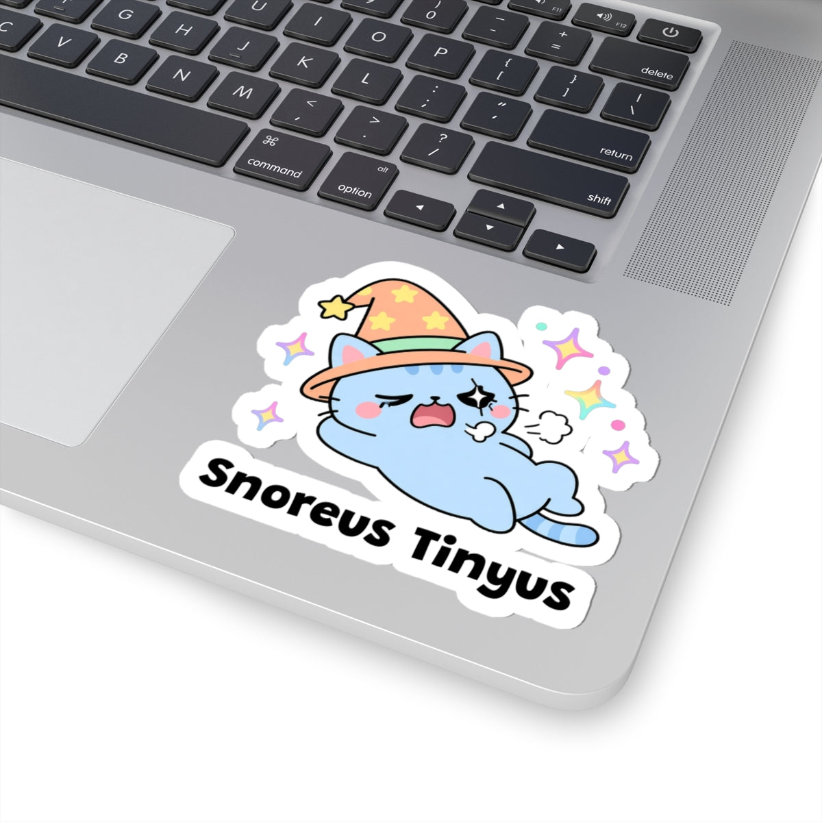 Snoreus Tinyus wizard cat sticker stuck on a silver laptop next to the keyboard