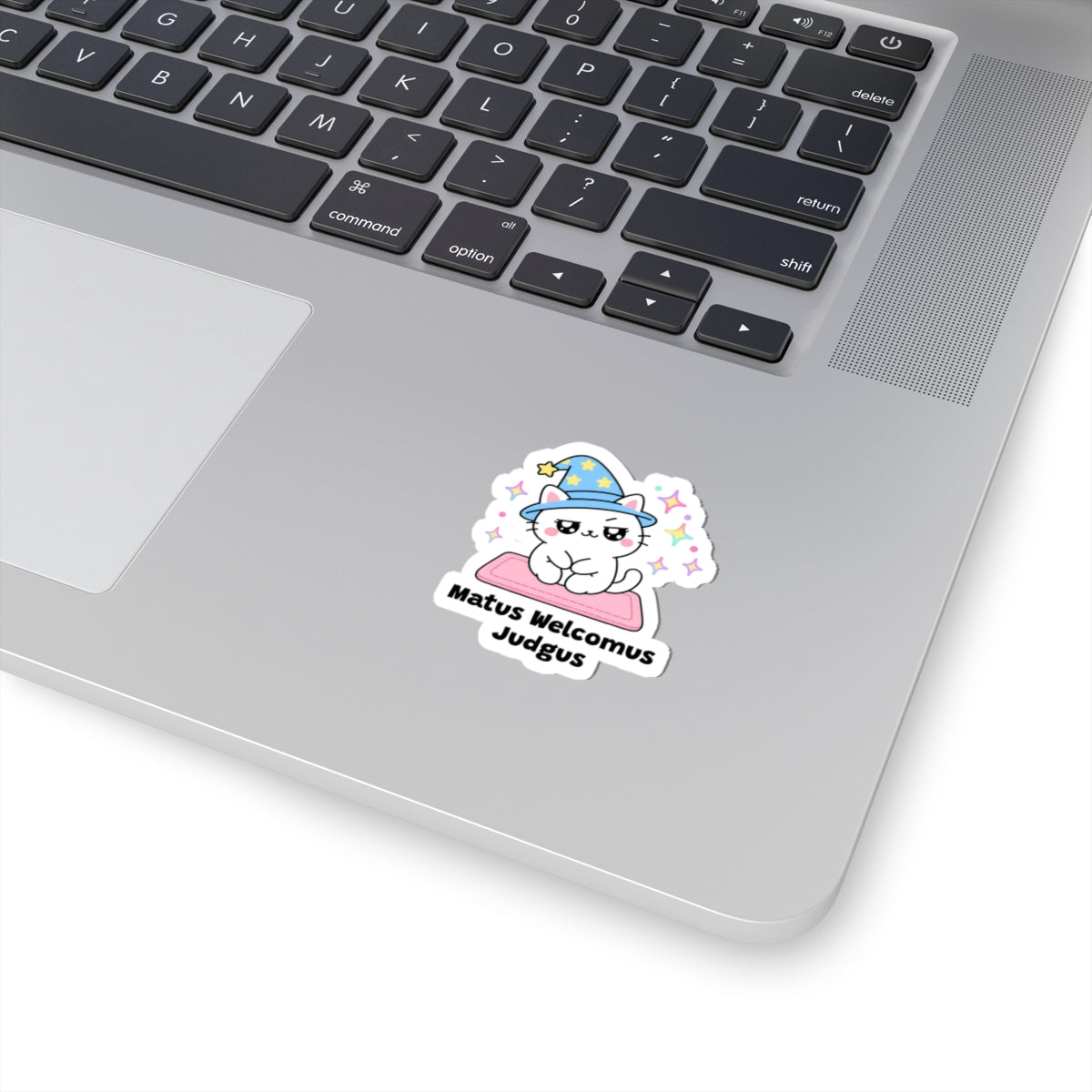 Matus Welcomus Judgus wizard cat sticker stuck on a silver laptop next to the keyboard