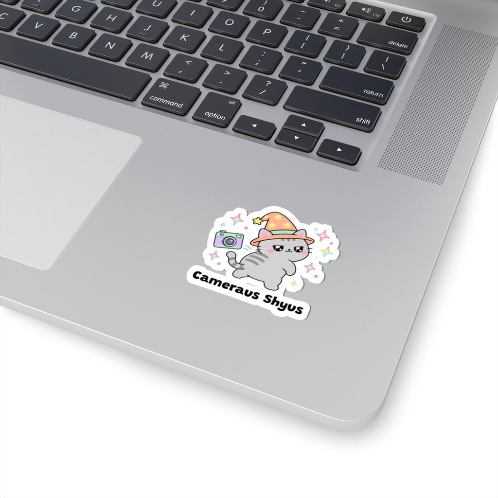Cameraus Shyus wizard cat sticker stuck on a silver laptop next to the keyboard