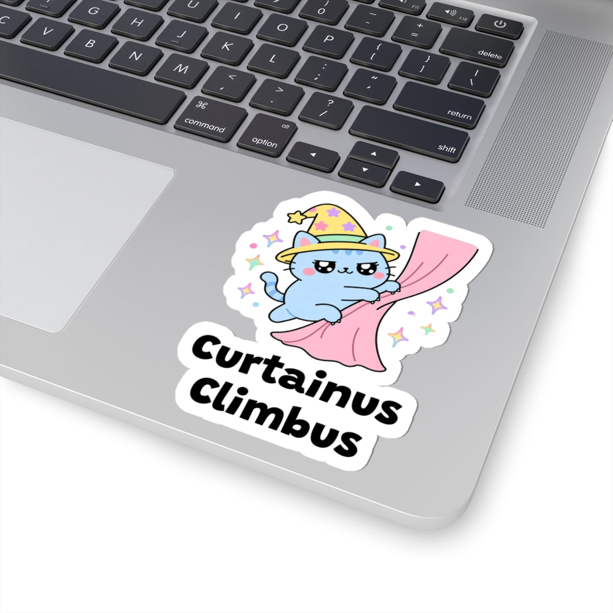 Curtainus Climbus wizard cat sticker stuck on a silver laptop next to the keyboard