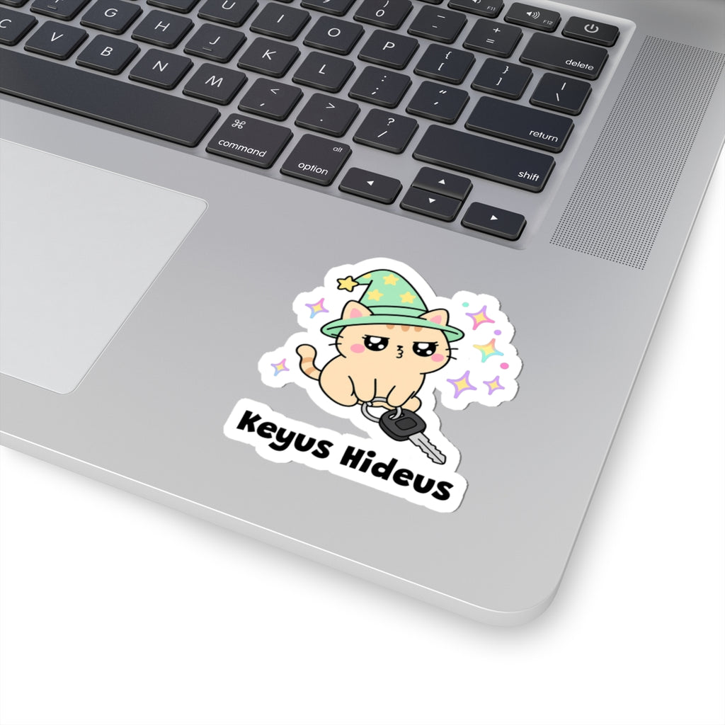 Keyus Hideus wizard cat sticker stuck on a silver laptop next to the keyboard