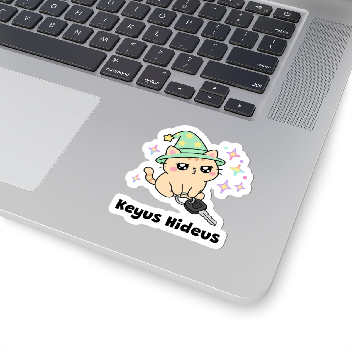 Keyus Hideus wizard cat sticker stuck on a silver laptop next to the keyboard
