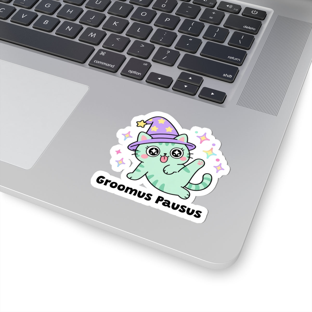 Groomus Pausus wizard cat sticker stuck on a silver laptop next to the keyboard