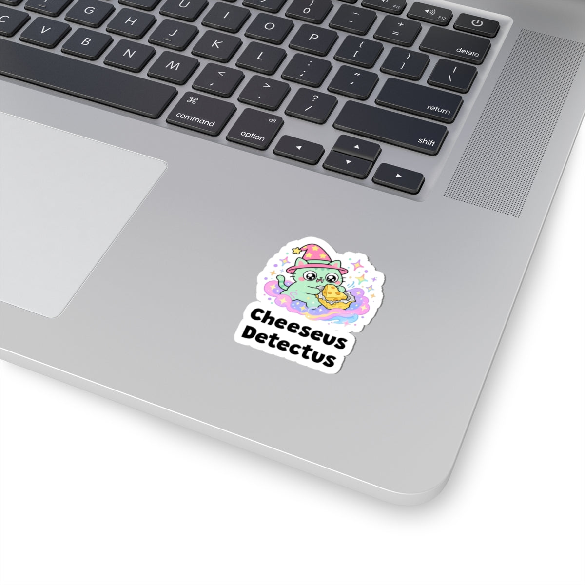 Cheeseus Detectus wizard cat sticker stuck on a silver laptop next to the keyboard
