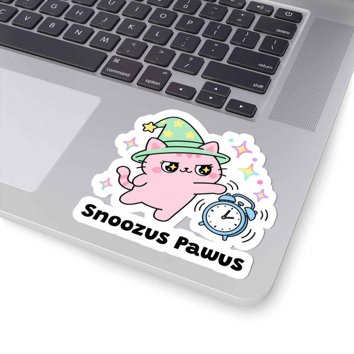 Snoozus Pawus wizard cat sticker stuck on a silver laptop next to the keyboard