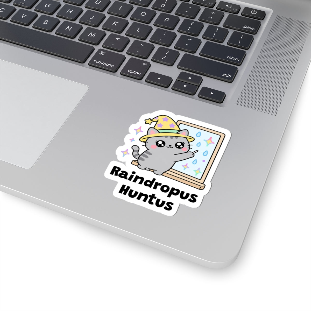 Raindropus Huntus wizard cat sticker stuck on a silver laptop next to the keyboard
