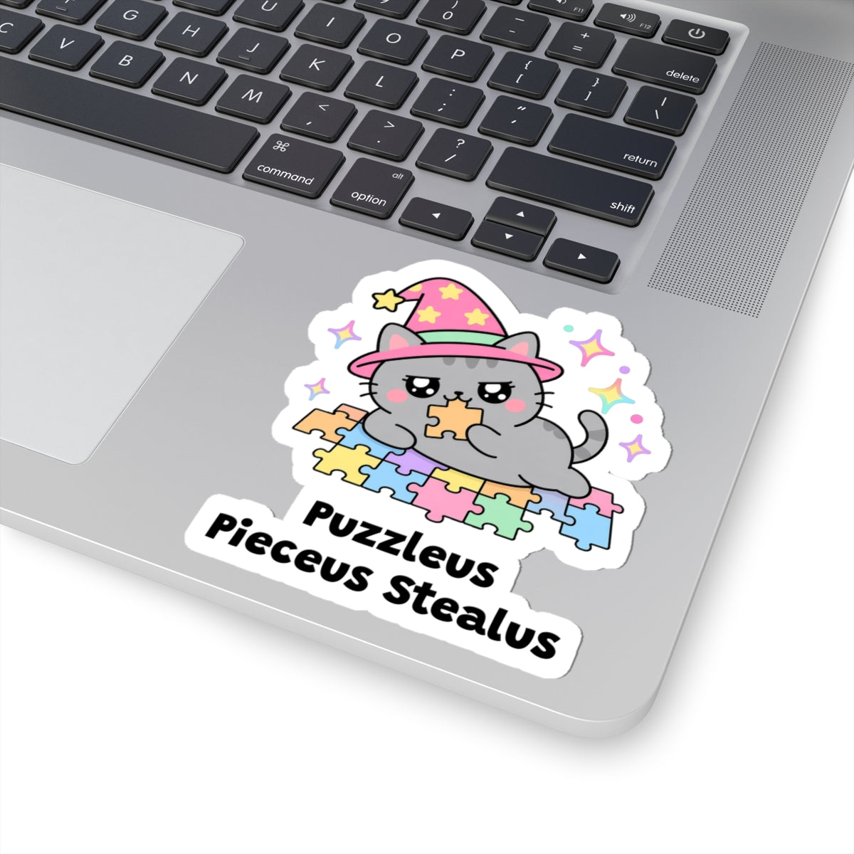 Puzzleus Pieceus Stealus wizard cat sticker stuck on a silver laptop next to the keyboard