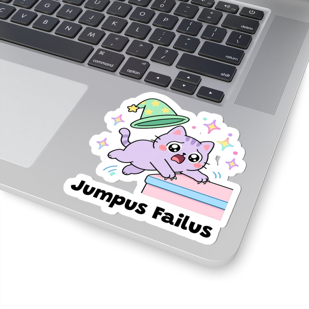 Jumpus Failus wizard cat sticker stuck on a silver laptop next to the keyboard