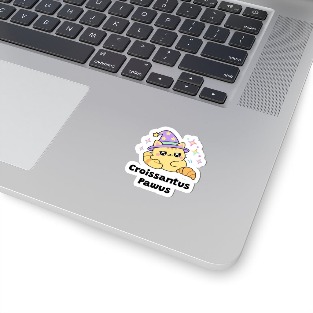 Croissantus Pawus wizard cat sticker stuck on a silver laptop next to the keyboard