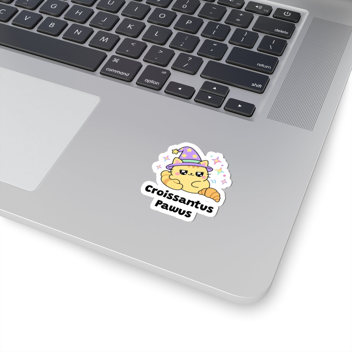 Croissantus Pawus wizard cat sticker stuck on a silver laptop next to the keyboard