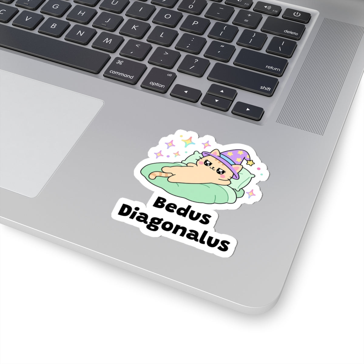 Bedus Diagonalus wizard cat sticker stuck on a silver laptop next to the keyboard