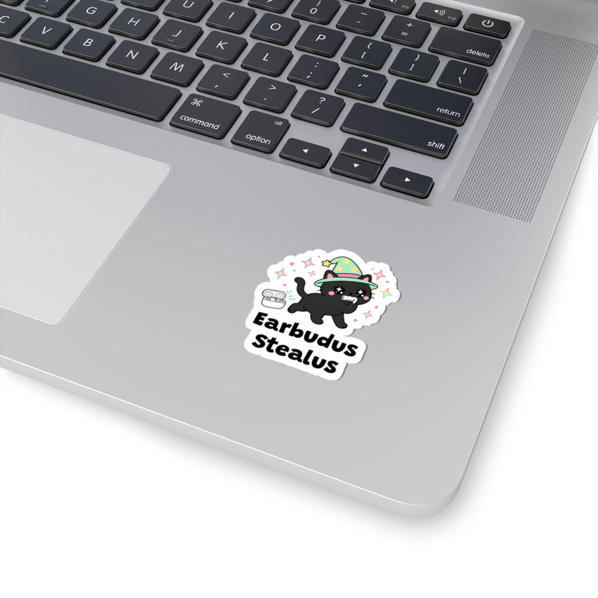Earbudus Stealus wizard cat sticker stuck on a silver laptop next to the keyboard