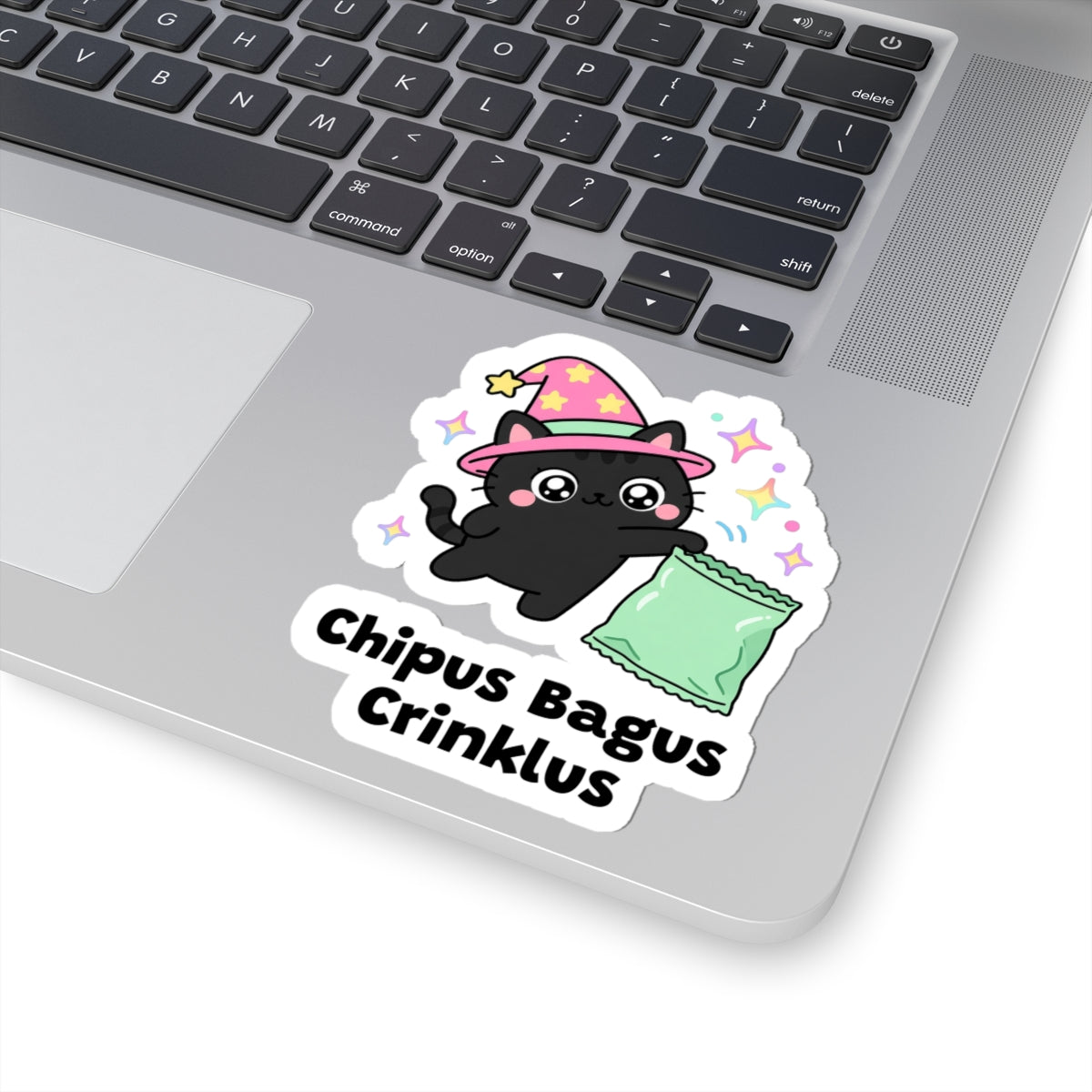 Chipus Bagus Crinklus wizard cat sticker stuck on a silver laptop next to the keyboard