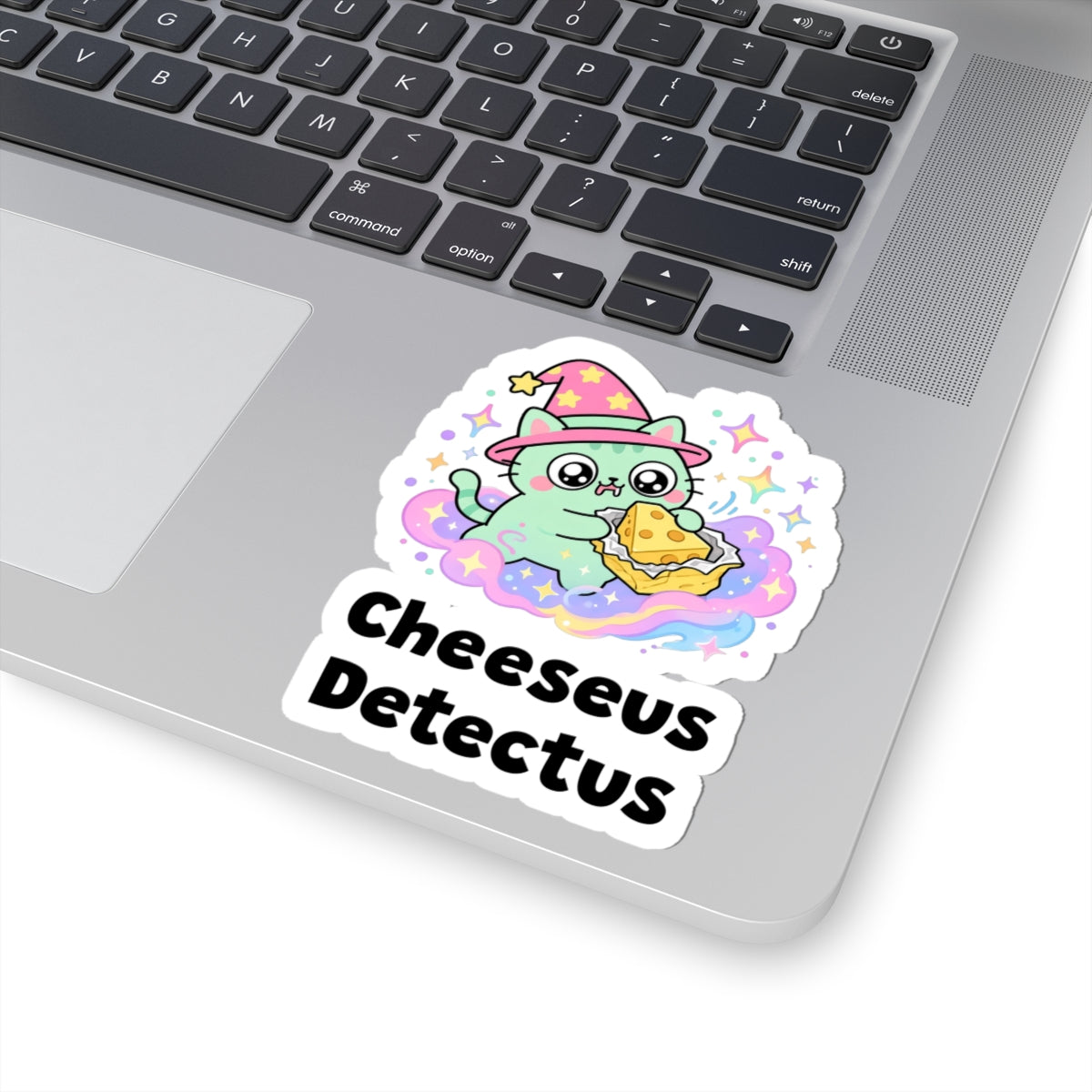 Cheeseus Detectus wizard cat sticker stuck on a silver laptop next to the keyboard