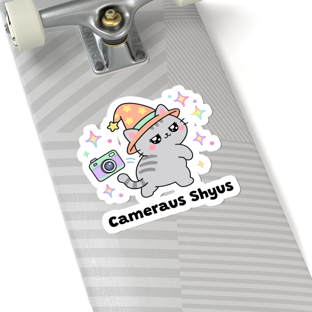 Cameraus Shyus wizard cat sticker on a grey skateboard deck near the truck