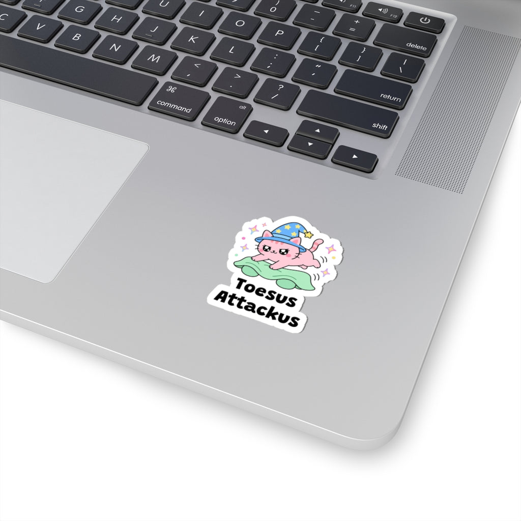 Toesus Attackus wizard cat sticker stuck on a silver laptop next to the keyboard