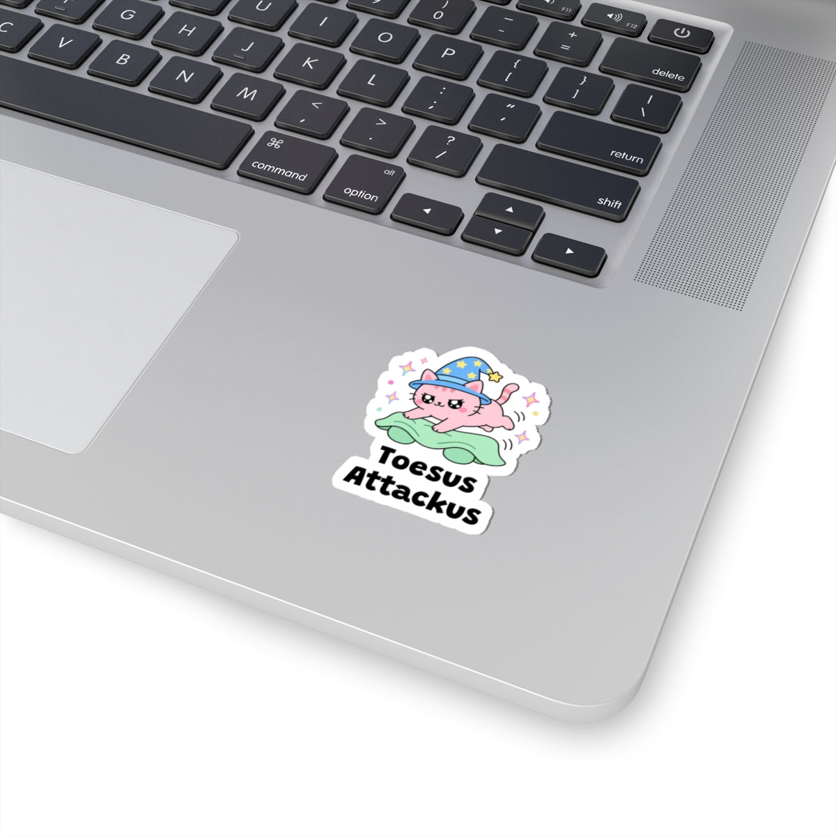 Toesus Attackus wizard cat sticker stuck on a silver laptop next to the keyboard