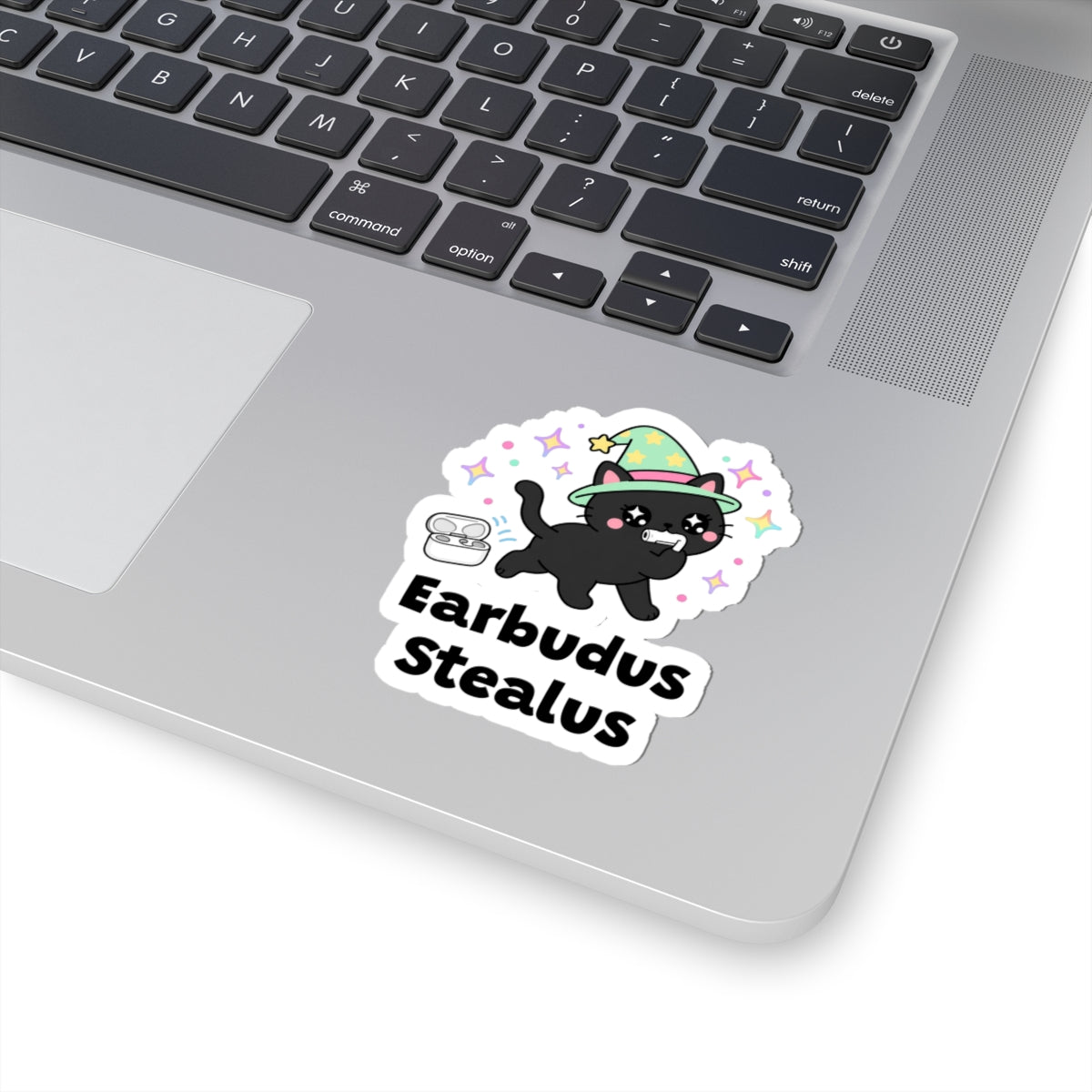 Earbudus Stealus wizard cat sticker stuck on a silver laptop next to the keyboard