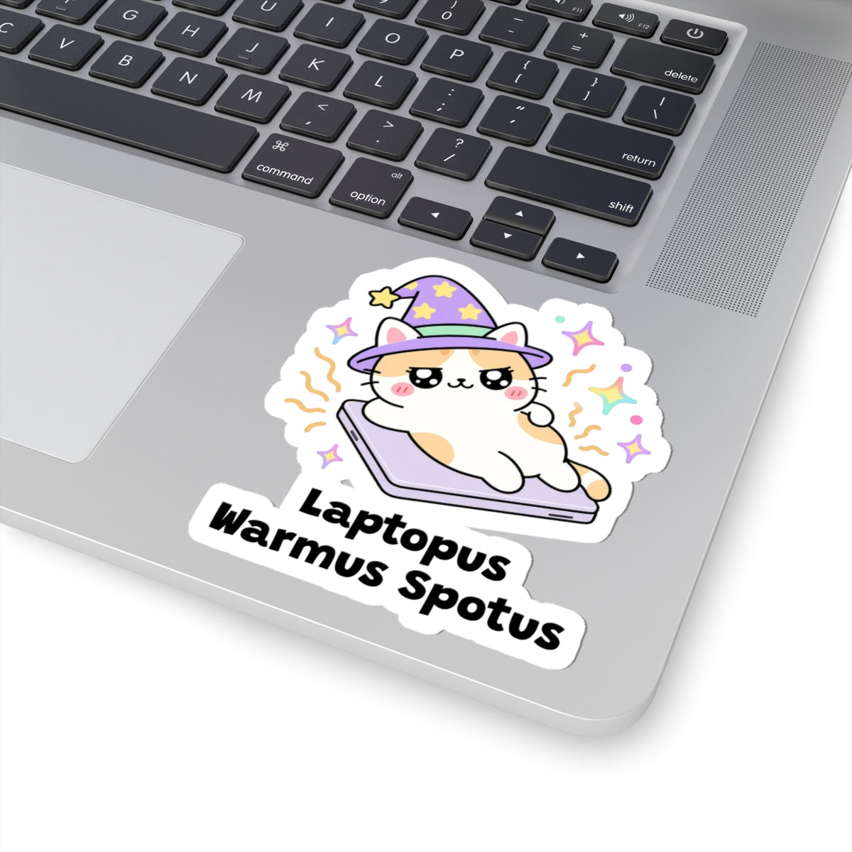 Laptopus Warmus Spotus wizard cat sticker stuck on a silver laptop next to the keyboard