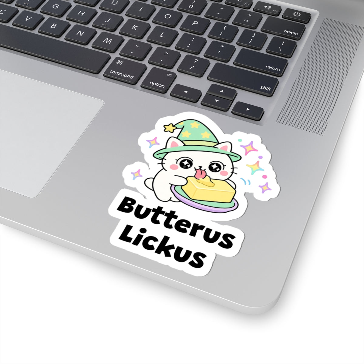 Butterus Lickus wizard cat sticker stuck on a silver laptop next to the keyboard