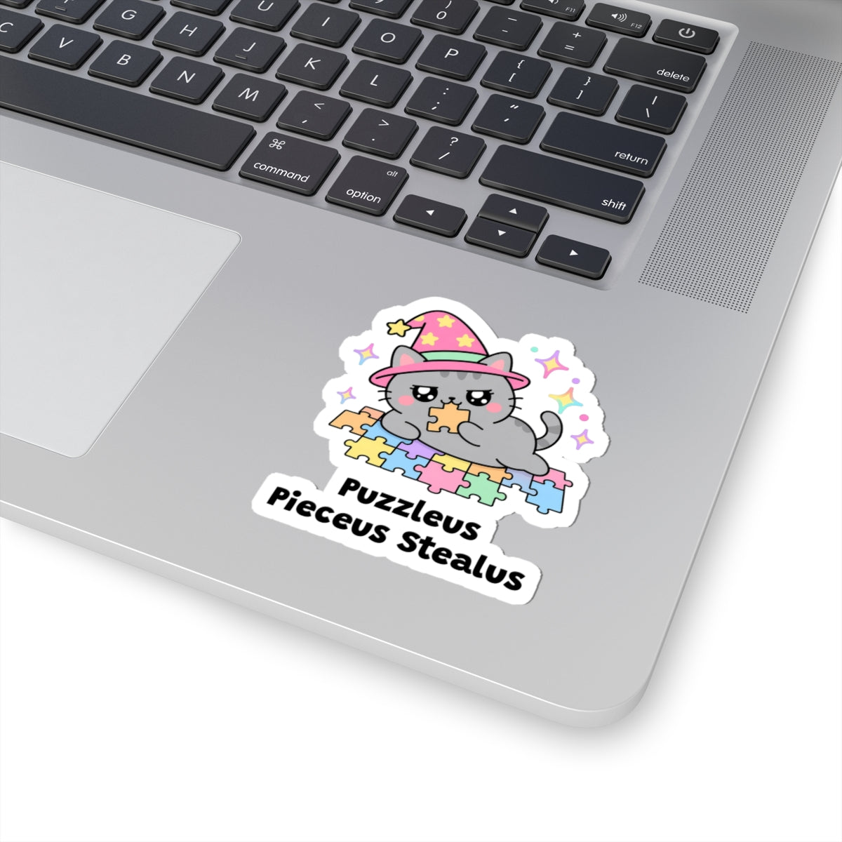 Puzzleus Pieceus Stealus wizard cat sticker stuck on a silver laptop next to the keyboard