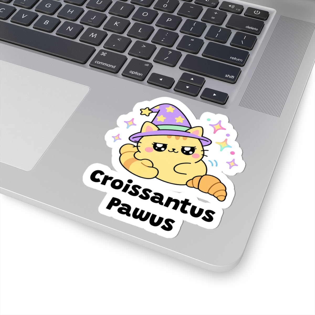 Croissantus Pawus wizard cat sticker stuck on a silver laptop next to the keyboard