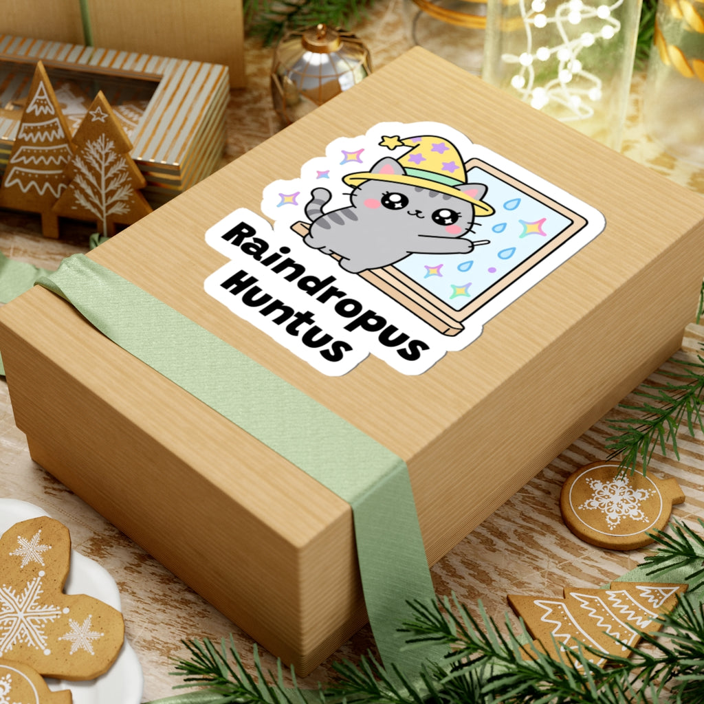 Raindropus Huntus wizard cat sticker on a kraft gift box with a green ribbon and holiday cookies