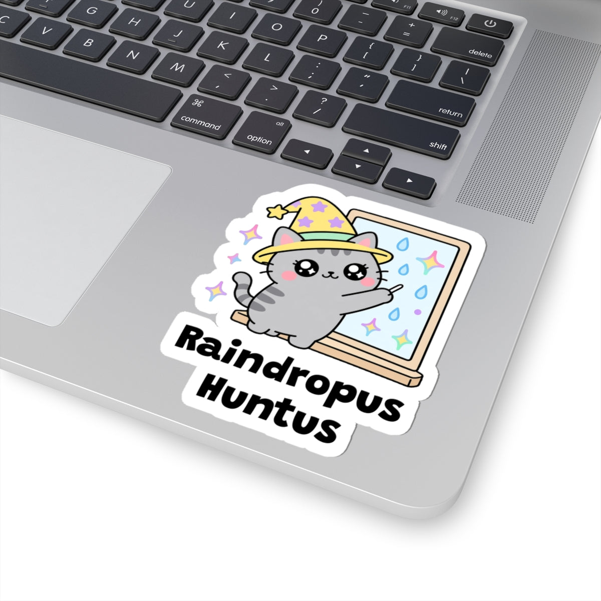 Raindropus Huntus wizard cat sticker stuck on a silver laptop next to the keyboard
