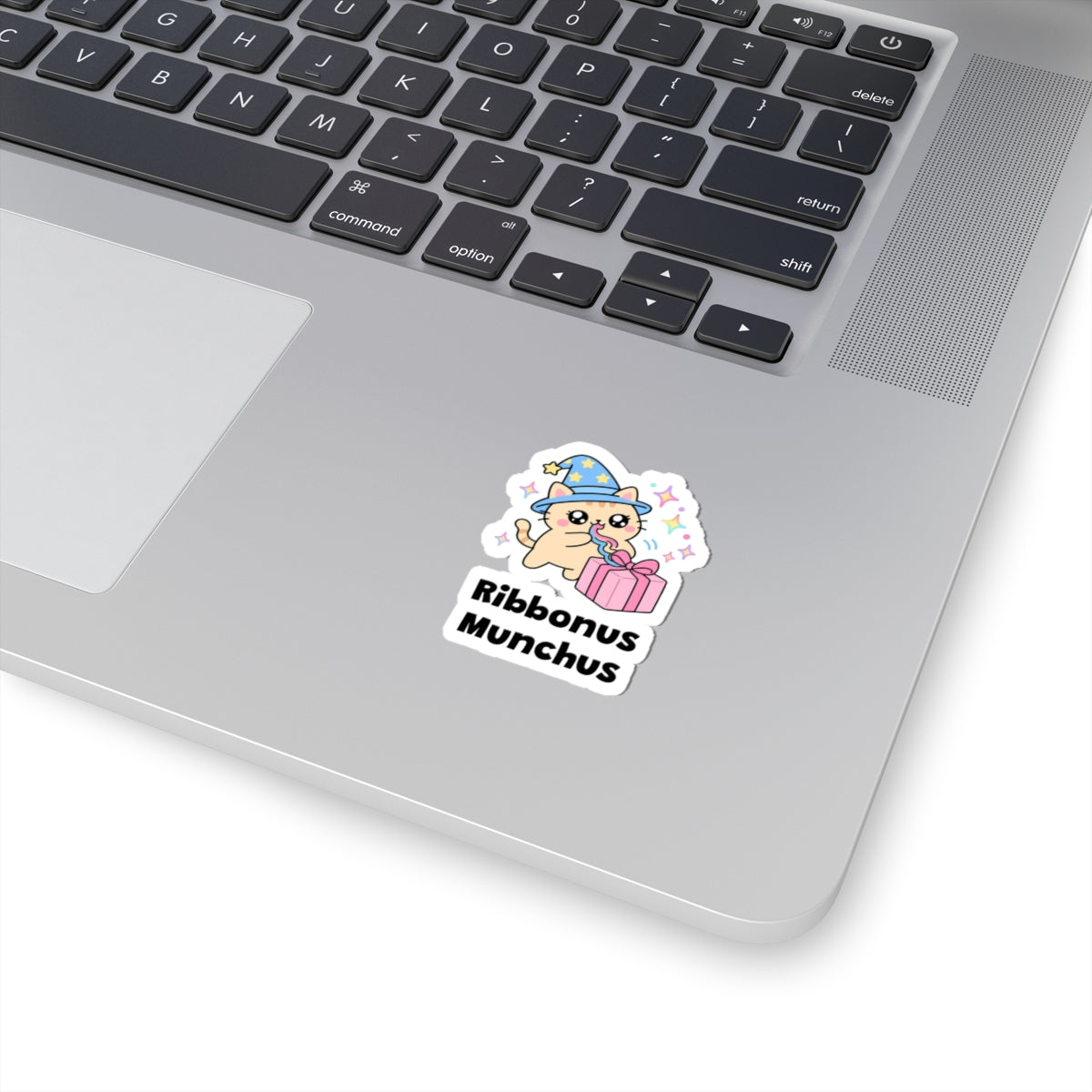 Ribbonus Munchus wizard cat sticker stuck on a silver laptop next to the keyboard